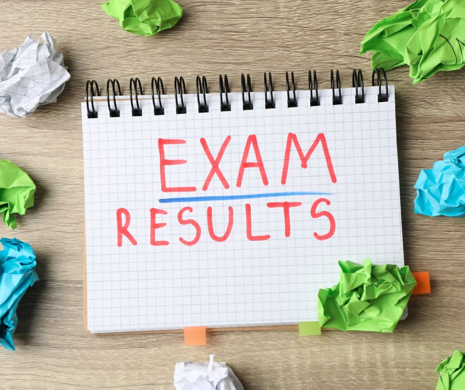 A notebook with the words 'EXAM RESULTS' written in red marker pen. Surrounding the notebook are scrunched up, coloured pieces of paper